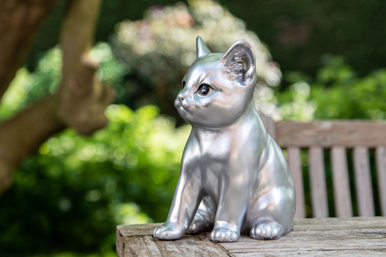 Statues of a modern silver cat standing on a wooden garden table Garden ID