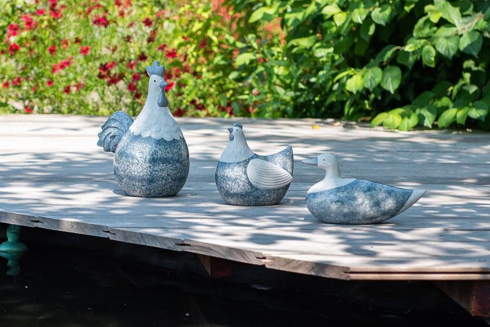 Blaustein-Effekt-Ornamente wie ein Hahn, eine Henne und eine Ente auf einer Holzterrasse an einem Teich Garden ID