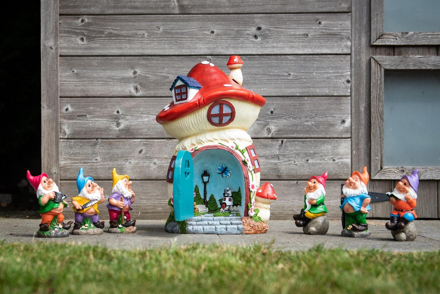 Six garden gnomes around their house with a door opening onto a terrace in front of a poolhouse Garden ID