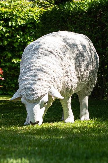 Een hyperrealistisch beeld van een wit schaap dat gras graast in een tuin Garden ID